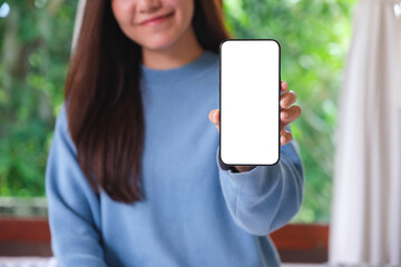 Mockup image of a woman holding and showing a mobile phone with blank white screen at home