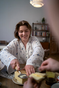 Smiling young woman scraping butter while sitting at table in home