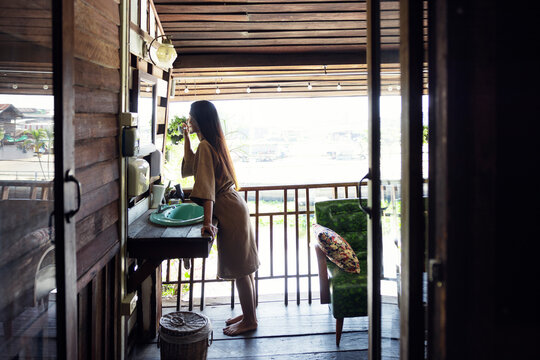 Side view of young woman brushing teeth while leaning on sink in cabin in Thailand