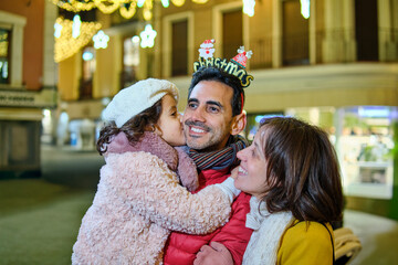 Father wearing Christmas headband kissed by daughter with smiling mother