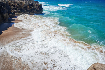 Shore and Sea. Sandy lonely beach with waves and ocean foam. Peaceful nature seascape. Beautiful summer scenery and rocks on the sand. Calm waves on the water