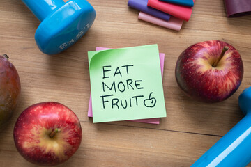 Green “Eat More Fruit” Sticky Note Surrounded by Fresh Fruit and Fitness Accessories