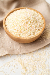 White sesame seeds in wooden bowl on natural linen cloth and white background. Organic sesame, cooking ingredient, Asian seasoning, source of calcium. Space for text