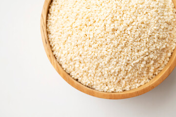 White sesame seeds in wooden bowl on white background. Organic sesame, cooking ingredient, Asian seasoning, source of calcium. Space for text