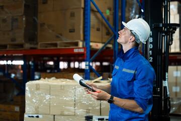 Warehouse personnel in protective helmet pointing and holding clipboard verifying stock against checklist inside packed warehouse environment promoting collaborative teamwork and operational unity