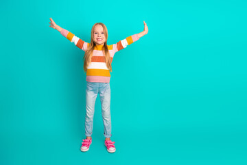 Smiling girl in casual striped sweater posing on turquoise background with happy expression and arms raised cheerfully