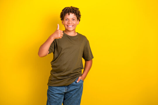 Cheerful young boy in casual khaki tshirt and jeans gives thumbs up against a bright yellow background ideal for promotion lifestyle and advertising - Powered by Adobe
