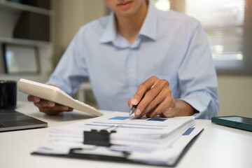 Close up of businessman using calculator and reviewing financial documents at office desk.