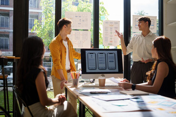 Group of designers discussing and reviewing mobile application prototypes laid out on the table during a creative brainstorming session.