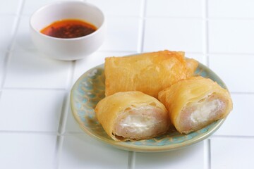 Crispy fried dim sum or dimsum goreng keju  served on a ceramic plate with chili sauce. Tasty Asian appetizer and popular Indonesian snack food photography in minimalist style.