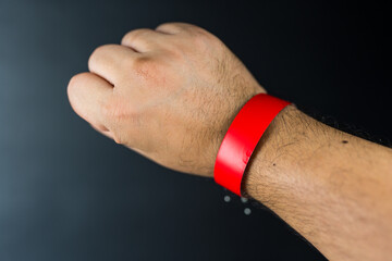 Male hand with a red paper wristband on a black background. Event ticket concept