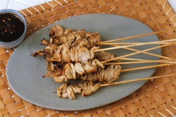 Close up of grilled mushroom skewers served on a plate with dipping sauce, delicious vegetarian street food snack.