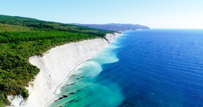 Flight over Cherno Sea coast. High layered rock with small pebble beach below. Trees grow above, Beautiful blue sea. Surf. Sunny weather