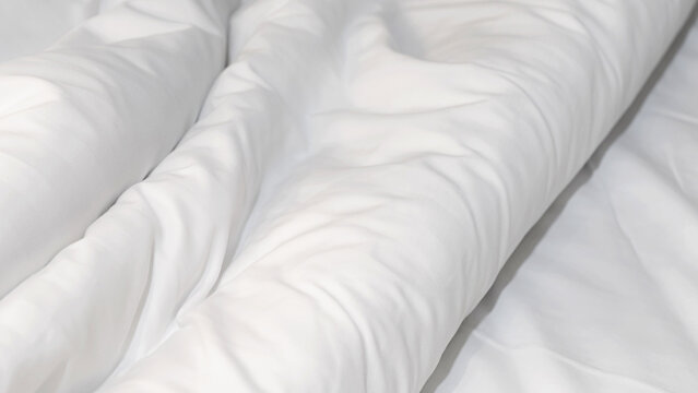 Close up soft white wrinkled duvet bed sheet texture, minimal background for comfort, cleanliness, and relaxation concept in bedroom or hotel interior