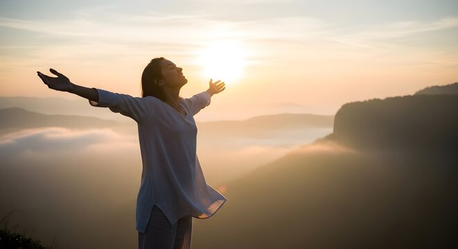 Woman standing on mountain with arms outstretched towards the sun, embracing nature and feeling free. Celebrating a spiritual connection with the world at sunrise, finding inner peace.