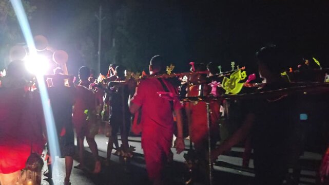 Nighttime footage of Kanwariya devotees dressed in saffron attire carrying decorated Kanwars Kawads during the sacred Shravan Somwar Sawan Monday pilgrimage in India. Illuminated by artificial lights