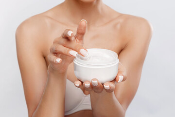 Woman applying moisturizer from a jar while holding it with one hand in a bright setting
