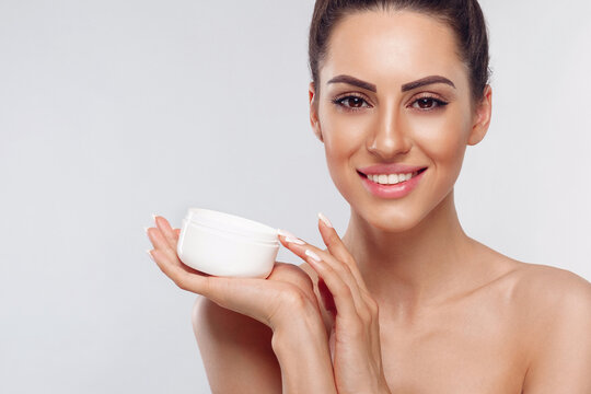 Smiling woman holding a skincare cream container against a light background during a beauty routine