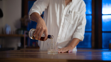 Man pouring whiskey into glass at night, warm light mood of relaxation and reflection.