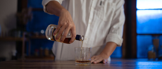 Man pouring whiskey into glass at night, warm light mood of relaxation and reflection.