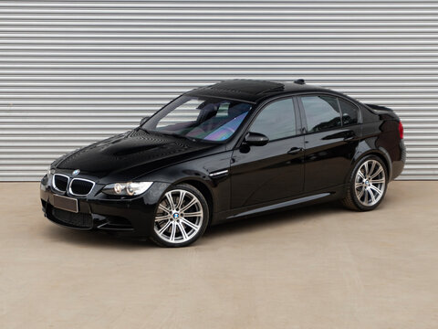 Black BMW M3 E90 in front of a metal wall, German V8 sports sedan front quarter view

