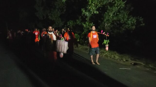 Nighttime footage of Kanwariya devotees dressed in saffron attire carrying decorated Kanwars Kawads during the sacred Shravan Somwar Sawan Monday pilgrimage in India. Illuminated by artificial lights