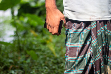 Man in lungi holding a phone in a lush green outdoor setting