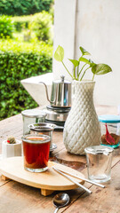 A tranquil scene of Vietnamese drip coffee or tea on a rustic wooden table with a white plant vase and lush green outdoor background