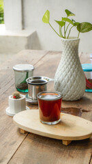 A tranquil scene of Vietnamese drip coffee or tea on a rustic wooden table with a white plant vase and lush green outdoor background