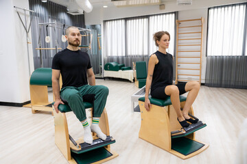 Fototapeta premium chair machine, Pilates exercises. exercises to strengthen body and stretch. practicing physical fitness exercises on Pilates machine. Reformer pilates machine for fitness workouts in gym studio