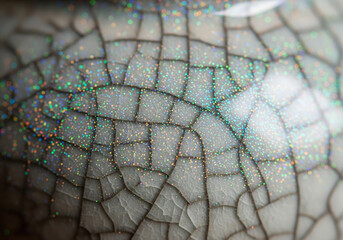 Close-up macro shot of a cracked ceramic surface with iridescent glitter sparkles, showcasing texture and light reflection