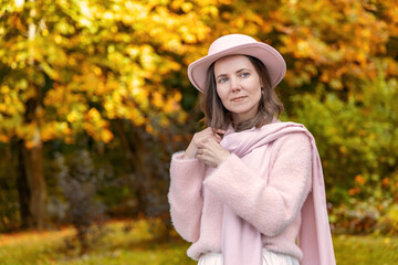 Female in pink hat and scarf posing outdoors in an autumn park wearing a soft fuzzy sweater