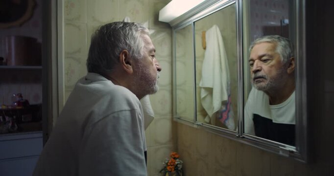 Older man gazing intensely at his reflection in bathroom mirror, confronting inner emotions and thoughts, a profound moment of self-reflection in a vintage tiled setting
