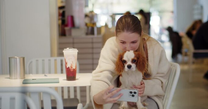 Woman taking selfie with cavalier spaniel in cafe