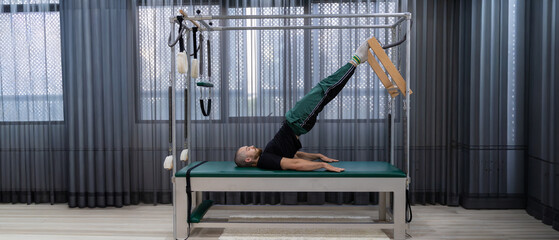Cadillac and reformer, caucasian man doing Pilates exercises to strengthen body and stretch....