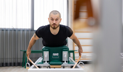 chest and back muscles, caucasian man doing Pilates exercises to strengthen body and stretch. practicing physical fitness exercises on Pilates machine. Reformer pilates studio machine for workouts