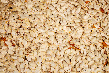 Pumpkin seeds scattered on a surface, showcasing their natural color and texture in bright lighting for culinary use and seasonal recipes