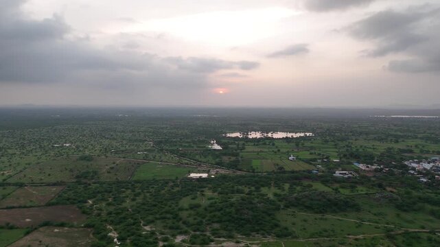 Aerial view of Padanga village, Ajmer, Rajasthan during monsoon sunset, showing lush green fields, ponds in the distance, cloudy sky, and native trees like Neem, Khejri, Babool, and Rohida