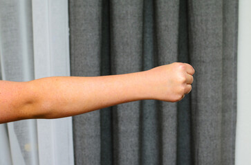 Human arm extended forward with clenched fist against modern neutral curtain background.