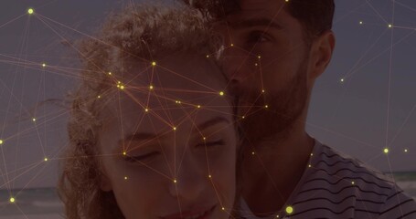 Leaning couple embracing at beach shoreline, man wearing striped shirt with yellow network overlay