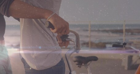 Person wearing striped shirt and jeans holding bike handlebars in seaside promenade, with railing