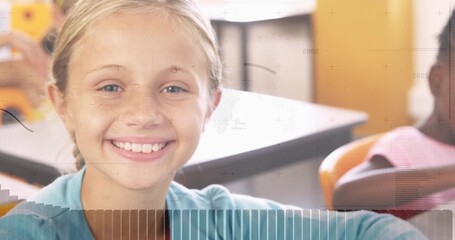 Smiling blonde student in light blue shirt sitting at school desk, with orange chairs, wall decor