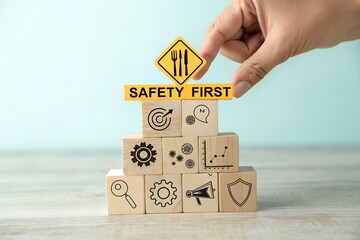 Hand places safety first sign on tower of wooden blocks with icons