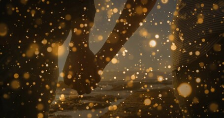 Holding hands couple wearing denim jeans and tees walking sandy beach at sunset, with golden bokeh