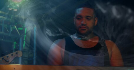 Performing male musician standing behind keyboard on dark stage, with colored lights and smoke haze