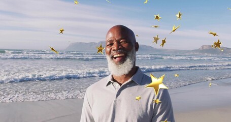 Smiling senior man in grey polo on sandy shore with rolling waves, golden star overlays floating