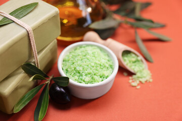 Handmade soap bars, olive, green leaves, sea salt and oil on coral background, closeup