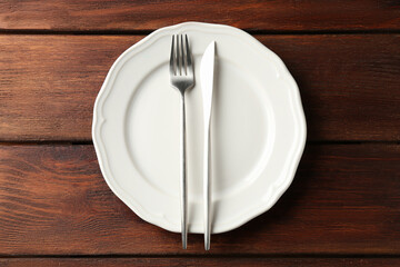 White ceramic plate and cutlery on wooden table, top view