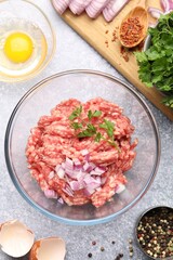 Raw minced meat with onion, parsley, spices and egg on grey table, flat lay