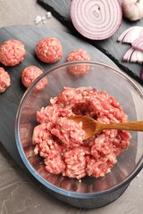 Raw meatballs, ground meat and onion slices on grey table, flat lay